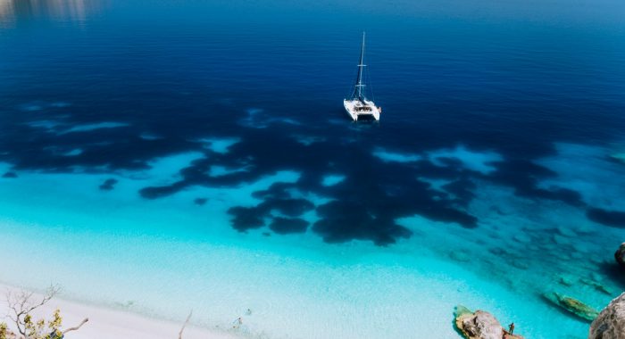White catamaran yacht drift on clear azure water surface in calm blue lagoon with transparent water and dark pattern on bottom White catamaran yacht drift on clear azure water surface in calm blue lagoon with transparent water and dark pattern on bottom.